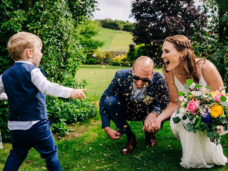 Boy throws confetti over bride and groom at Pangdean Old Barn wedding