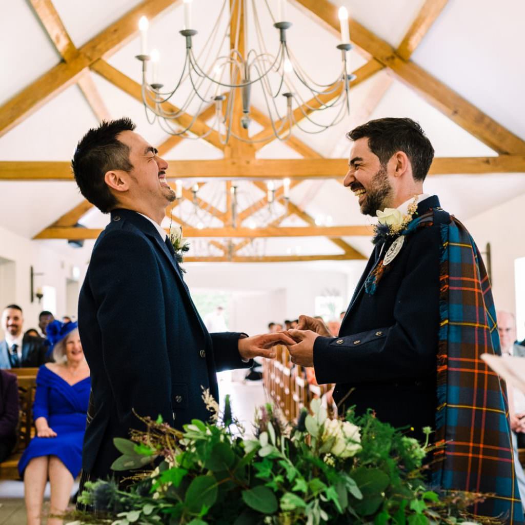 Two grooms laugh as they exchange wedding rings - Oaks Farm Weddings