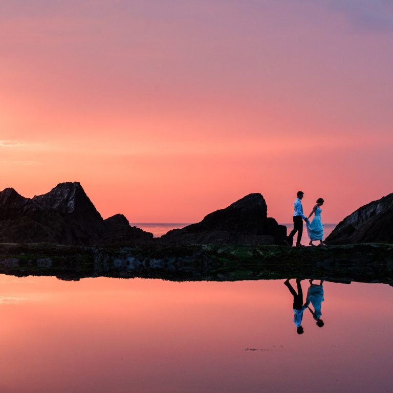 Bride and groom reflected in tidal pool at Tunnels beaches wedding at sunset