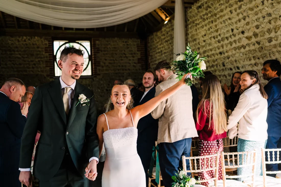 Happy bride raises her bouquet in the air comng down the aisle