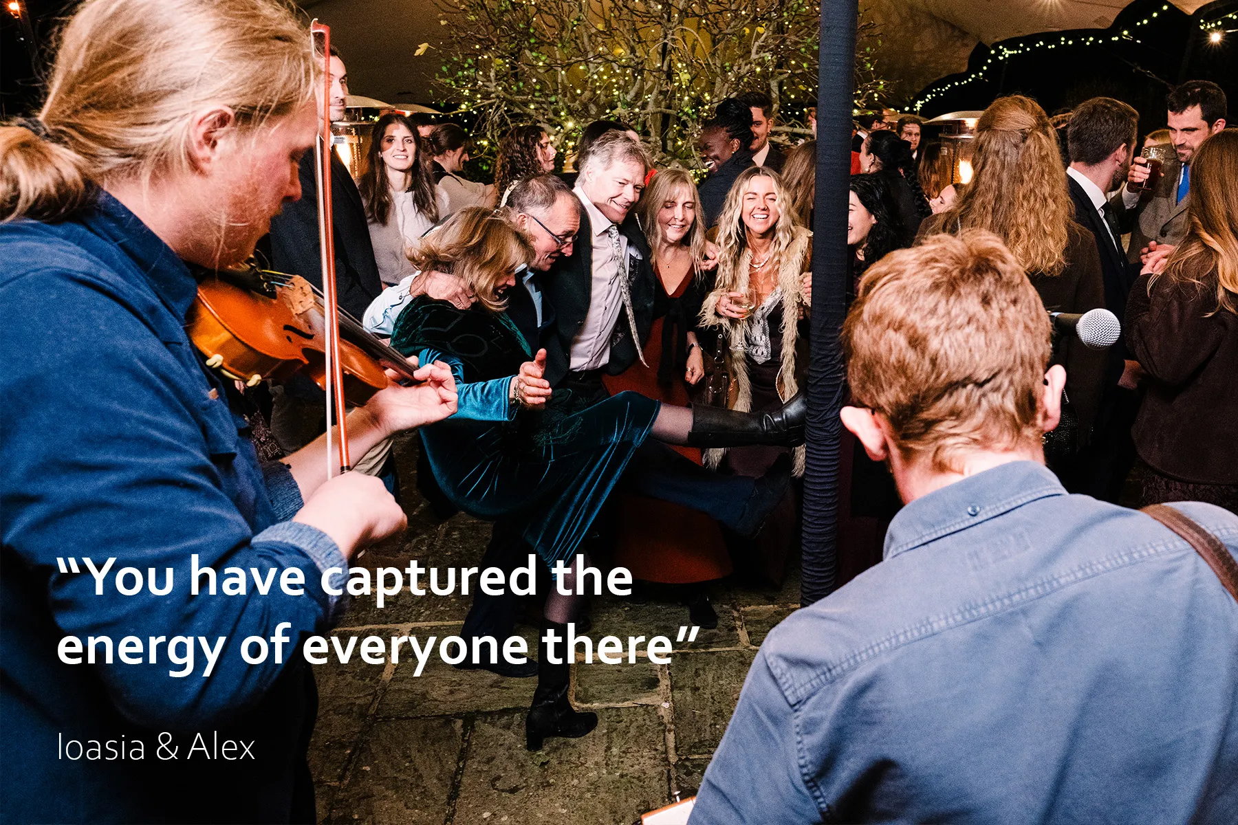 Guests dance to live music with a violinist and guitarist under a tipi at festival-style Sussex wedding